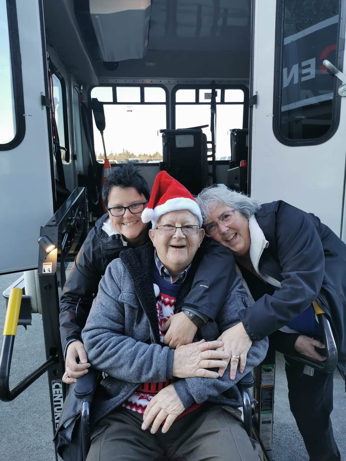 Susan and Dianne posing with male client in wheelchair on accessible bus ramp